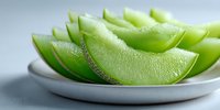 Fresh green honeydew melon slices arranged on white ceramic plate, showcasing juicy texture and vibrant color for food photography and healthy eating concepts.