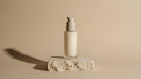 Beige cosmetic serum bottle with pump dispenser on textured stone block against neutral background for skincare and beauty product marketing.