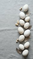 Natural Easter eggs with feathers and decorative elements arranged on gray linen background for spring holiday celebration and seasonal greeting cards.