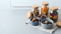 Healthy snack collection with nuts, dried fruits and seeds in glass jars and ceramic bowls on kitchen counter for nutritious eating and meal prep.