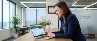 Professional businesswoman working on laptop in modern office environment with natural lighting and contemporary workspace design.