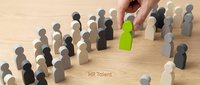 Human resource manager selecting green wooden figure among gray and black figures on wooden surface, representing talent recruitment and employee selection process.
