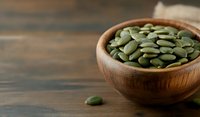 Raw green pumpkin seeds in wooden bowl on rustic dark table background with copy space. Natural organic superfood for healthy eating and snacking.