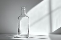 Empty glass bottle with dramatic window light and shadow casting geometric shapes on minimal gray background, artistic still life composition.