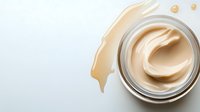 Creamy beige foundation makeup in glass jar with smooth texture swirl and cosmetic smear on white background for beauty and skincare products.