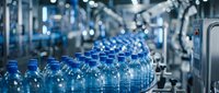 Rows of blue plastic bottles moving along an automated conveyor belt in a modern beverage manufacturing facility, showcasing industrial production and packaging technology.