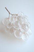 Translucent glass grape cluster with metallic stem on white background, minimalist artistic still life composition for modern interior decor and design projects.