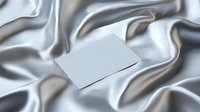 Blank white card mockup on luxurious silver silk fabric with elegant folds and waves creating soft shadows. Minimalist design layout for branding presentation.