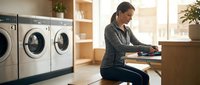Young Asian woman folding clean laundry in modern laundromat with washing machines. Domestic chores and household tasks concept for lifestyle content.