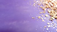 Scattered gold metallic glitter flakes on purple gradient background with soft bokeh effect and copy space for luxury design projects.