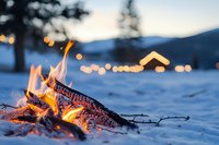 Cozy campfire burning in snowy winter landscape at dusk with warm flames and glowing embers creating peaceful outdoor atmosphere for camping adventures.