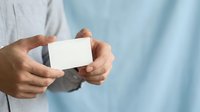 Man in light blue shirt holding blank white business card, ready for contact information or branding mockup design.