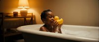 Happy African American woman relaxing in bathtub with rubber duck toy in warm cozy bathroom setting with soft lighting for wellness and self-care concepts.