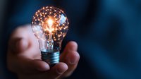 Glowing light bulb with illuminated filament held in hand against dark background, symbolizing innovation, creativity and bright ideas for business concepts.