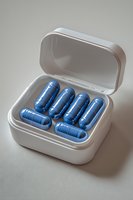 Blue medical capsules in white plastic container on neutral background. Pharmaceutical and healthcare concept for drug prescription and medication.