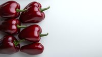 Fresh red sweet peppers arranged on white background, glossy burgundy bell peppers with green stems creating minimalist composition for food photography.