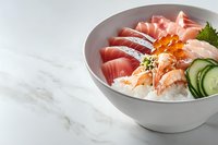 Fresh sashimi and seafood bowl with tuna, salmon, shrimp, red caviar, cucumber slices and steamed rice on white marble background with copy space.