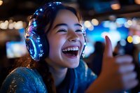 Young Asian woman wearing illuminated LED headphones laughing joyfully at night with bokeh lights in background, showing thumbs up gesture in entertainment setting.
