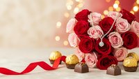 Romantic bouquet of red and pink roses with golden heart chocolates and red ribbon on warm bokeh background for Valentine's Day celebrations.