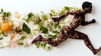 Running silhouette made from dark chocolate sprinkled with nuts, decorated with fresh green lettuce leaves and citrus, creative food art composition.