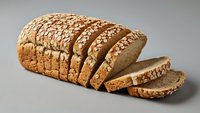 Freshly sliced whole grain bread loaf with seeds and oats, perfect for healthy breakfast, sandwiches and bakery products on neutral background.