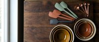 Modern kitchen utensils and ceramic bowls in earth tones arranged on rustic wooden surface for cooking and food preparation styling.