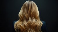 Long wavy blonde hair from behind against dark background showcases professional hairstyling with natural highlights and dimensional color movement.