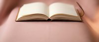 Open book with blank pages on soft pink surface with warm lighting for reading and education concepts.