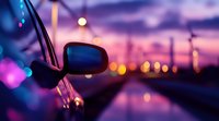 Side mirror of car at sunset with blurred city lights creating dreamy bokeh effect on urban road, purple and orange sky reflects on wet surface.