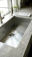 Modern undermount kitchen sink with water droplets in granite countertop near window with natural light and potted plants for contemporary home design.