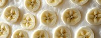 Fresh sliced bananas arranged in neat rows on white surface showing star pattern centers, macro food photography highlighting natural fruit texture and pattern.