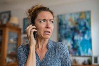 Frustrated middle-aged Caucasian woman talking on phone with worried expression in modern home interior for communication and stress concepts.