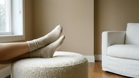 Woman relaxing with feet up on ottoman in cozy living room with neutral beige walls and white furniture for comfort and leisure lifestyle.