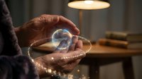 Elderly hands holding a glowing crystal ball with magical light particles in a cozy dimly lit room, evoking mystery and fortune telling.