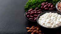 Fresh cottage cheese in black bowl with red kidney beans and raw almonds on dark stone background, healthy protein food ingredients.