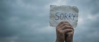 Hand holding handwritten sorry sign against cloudy sky background expressing apology regret forgiveness concept for emotional communication.