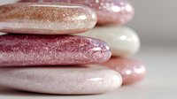 Smooth stacked stones in shimmering pink, rose gold, and pearl white tones creating a zen-like balance on neutral background.