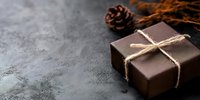 Chocolate gift box with natural twine bow on dark textured surface with autumn leaves and pine cone for holiday celebrations and special occasions.