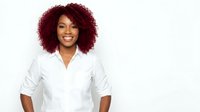 Smiling African American woman with curly red hair in white button-up shirt on light background for business and professional marketing materials.