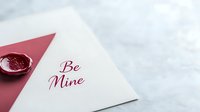Romantic Valentine's day card with red wax seal and elegant "Be Mine" calligraphy text on white paper against light marble background, love letter concept.