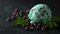 Mint chocolate chip ice cream scoop garnished with fresh mint leaves and chocolate chips on dark background, dramatic lighting creates appetizing mood.