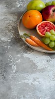 Fresh colorful fruits and vegetables on ceramic plate against textured gray background. Grapefruit, orange, apple, grapes and carrots composition for healthy eating concept.