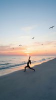Woman practicing yoga warrior pose on beach at sunset with seagulls flying overhead. Peaceful meditation and wellness lifestyle concept for mindfulness and fitness.