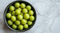 Fresh green key limes in rustic ceramic bowl on white marble background, overhead view. Natural light food photography for culinary and recipe content.
