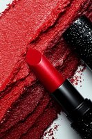 Red lipstick with smeared makeup textures and scattered pigment powder creating artistic cosmetic composition for beauty and fashion concepts.