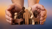 Protective hands sheltering wooden family figures and pets against sunset sky. Insurance, care, security and family protection concept for design.