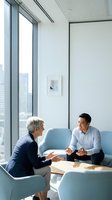 Two business professionals having productive meeting in modern office with city skyline view through floor-to-ceiling windows and contemporary furniture.