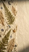 Pressed dried fern leaves and small blue flowers arranged on textured handmade paper background for botanical art and natural craft projects.