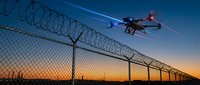 Security drone with searchlight flying over prison fence with barbed wire during sunset surveillance operation for border control and facility monitoring.