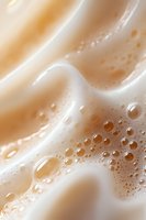 Creamy coffee foam macro with golden bubbles and swirls creating abstract patterns against soft beige background, showing rich texture and depth.